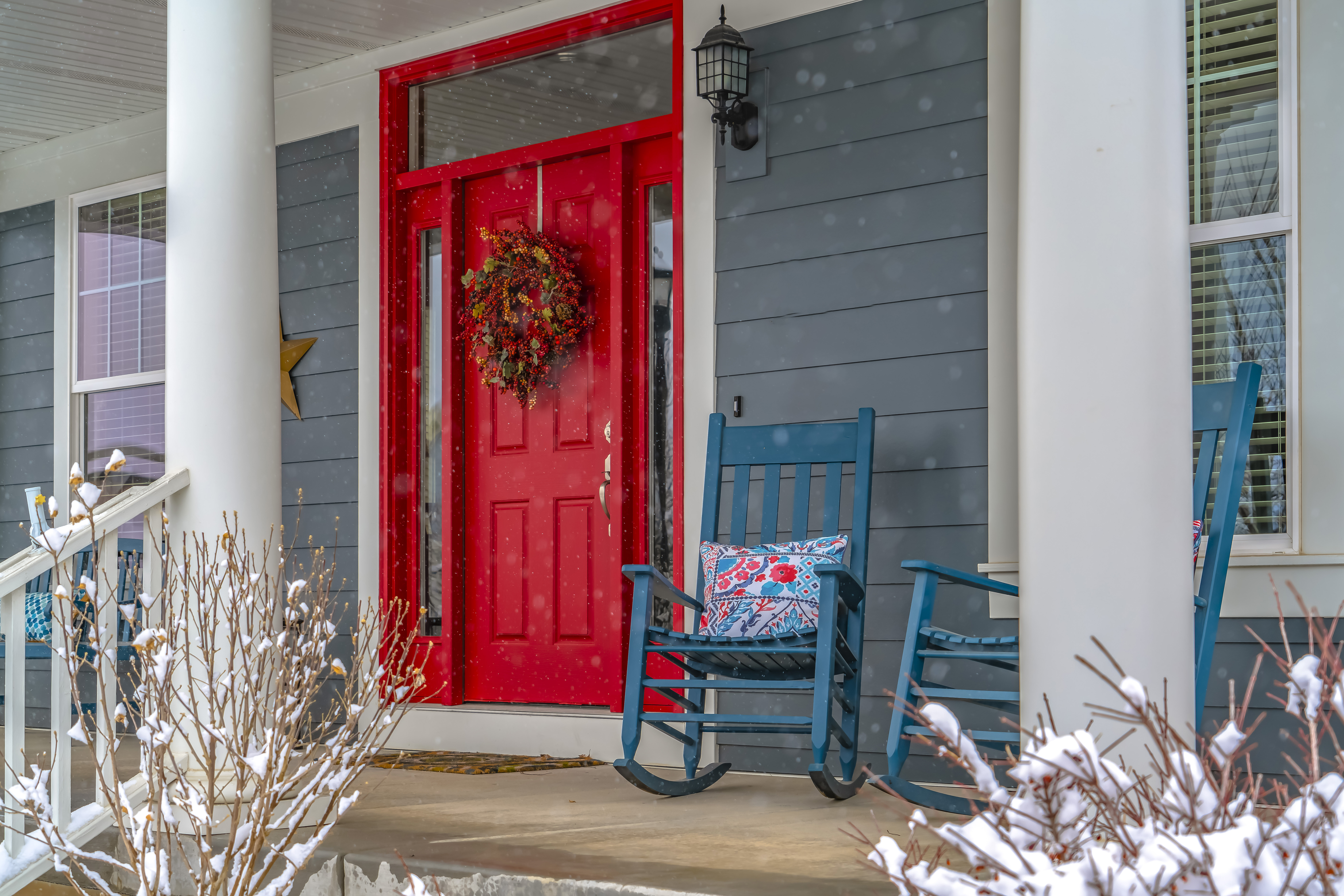 sideview of a home's porch in winter. red front door. rocking chairs.
