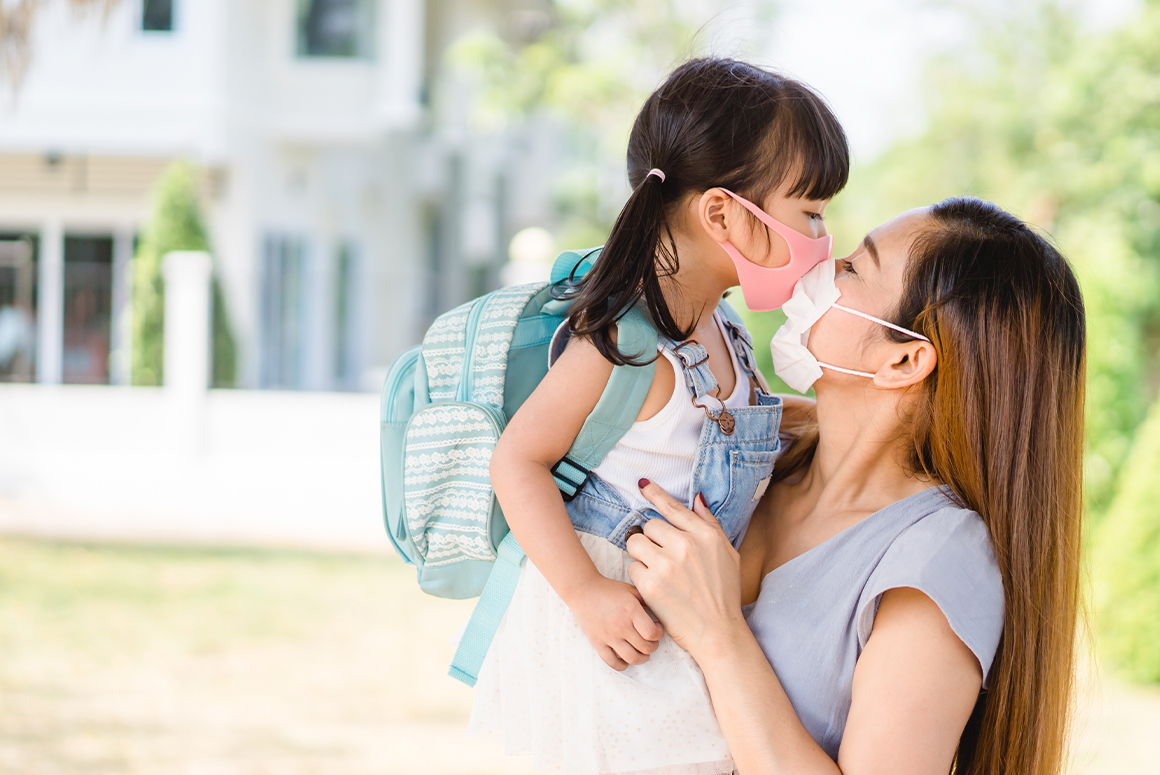 mom holding daughter, both wearing masks and looking at each other