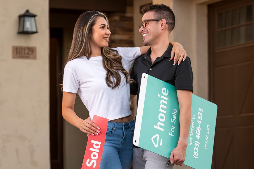 young couple holding their sold homie sign in front of their new home