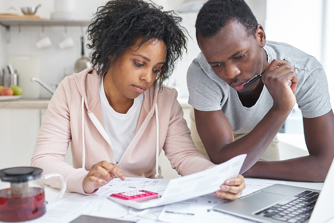 black couple over a computer with paperwork, calculating the cost of selling their home