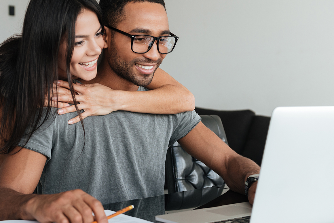 couple sitting at a desk, looking at a laptop together