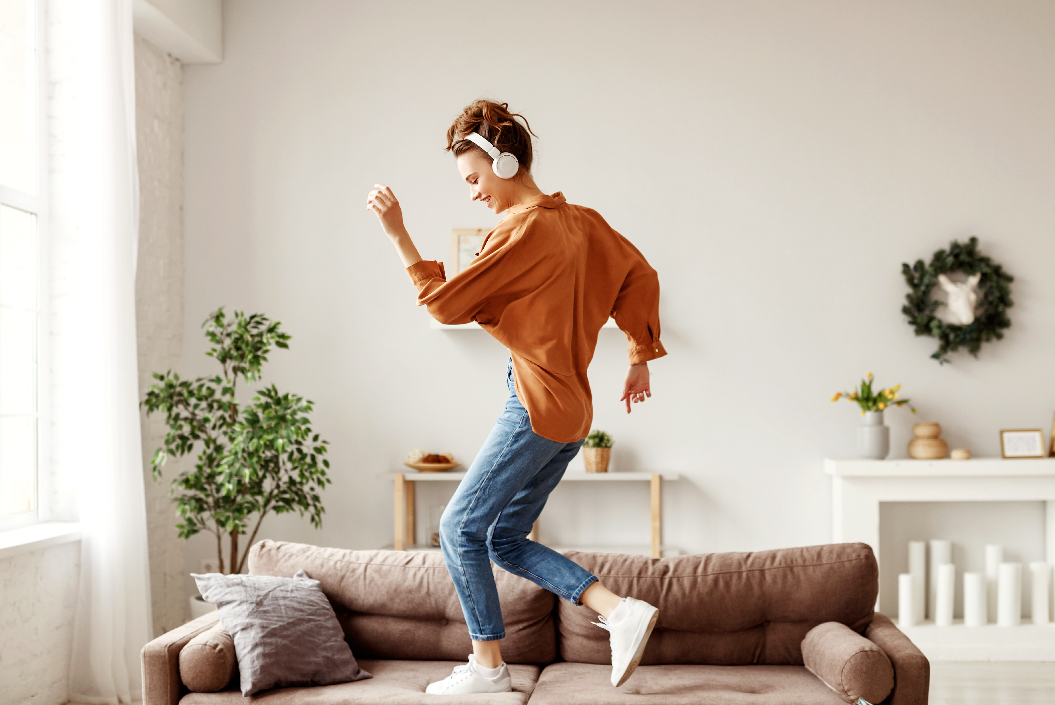 woman listening to headphones, jumping on a couch