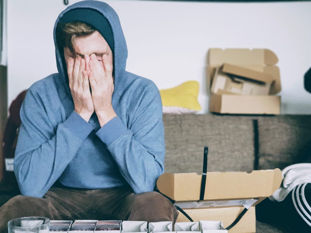man surrounded by moving boxes hiding his face in his hands