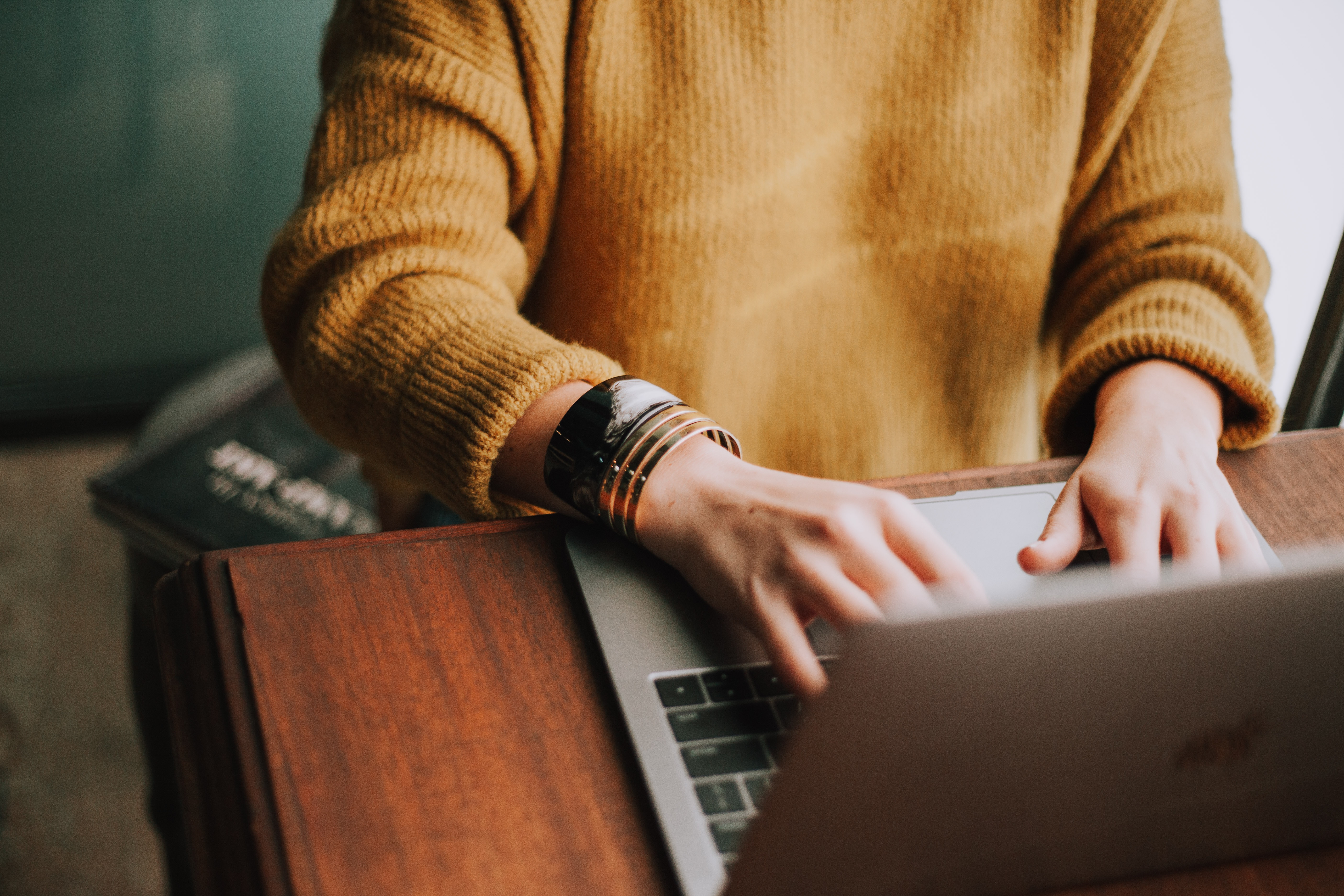 woman in mustard sweater using laptop to browse