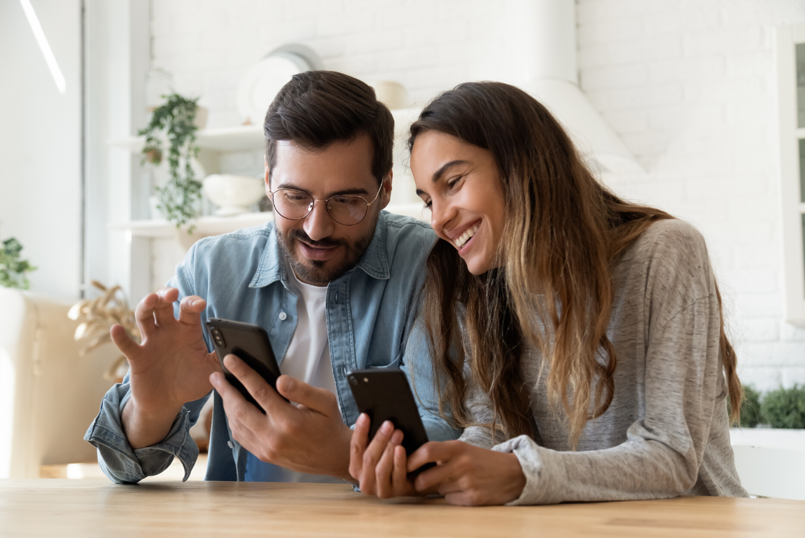 couple sitting at kitchen table, looking at smart phones together