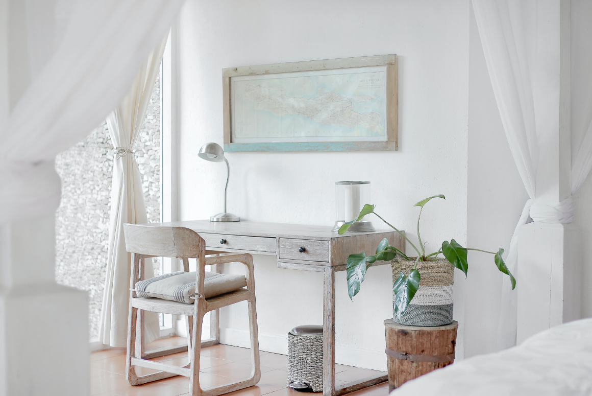 work from home office in bedroom with white desk, walls, and a plant